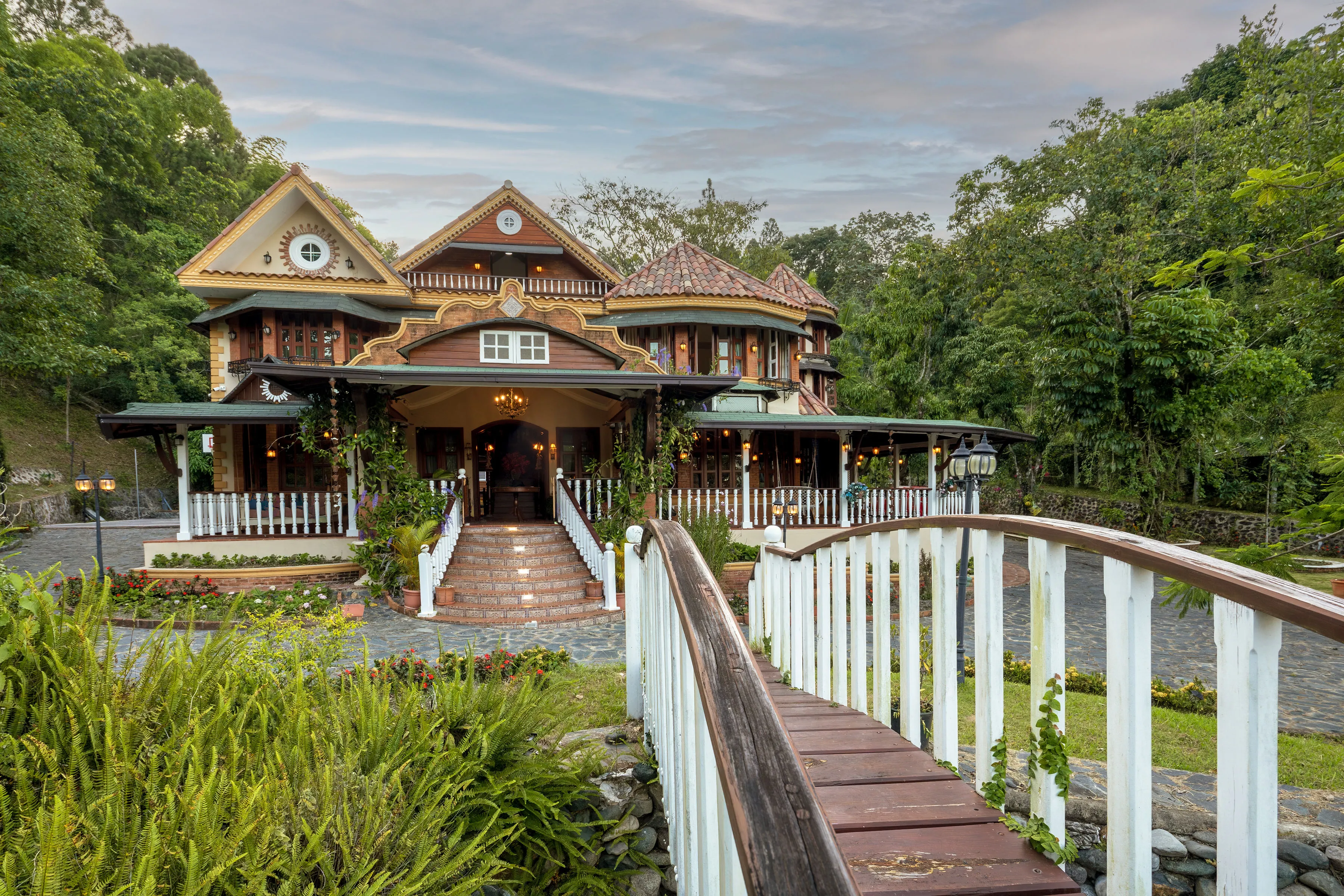 The house and entry bridge at dusk, framed by gardens and mountain forest
