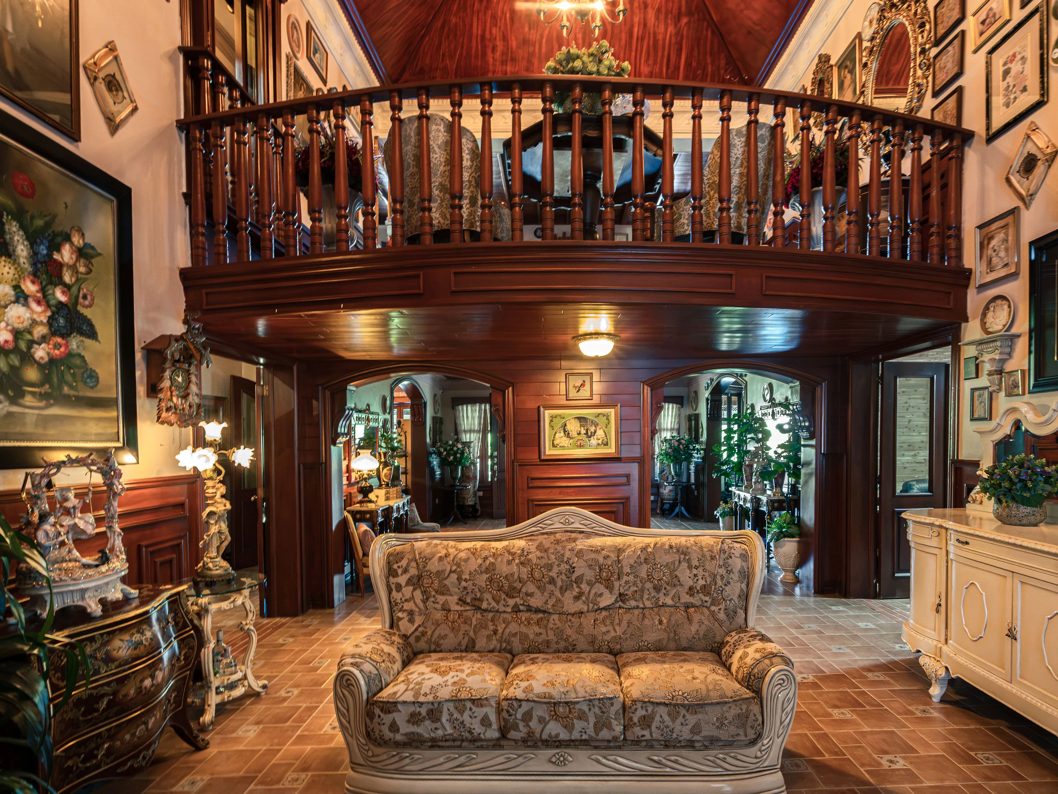Double-height living room with a mahogany mezzanine, chandelier, and antique furnishings