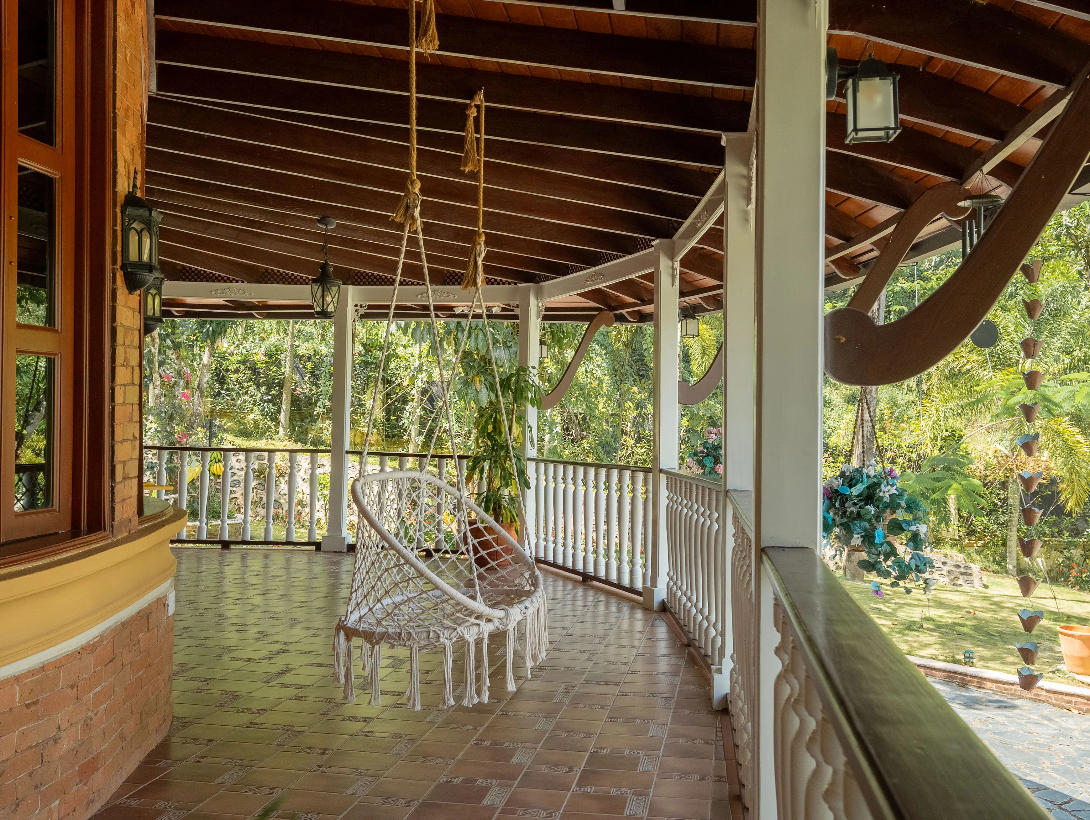 Wraparound porch with a hanging macramé swing chair overlooking the garden